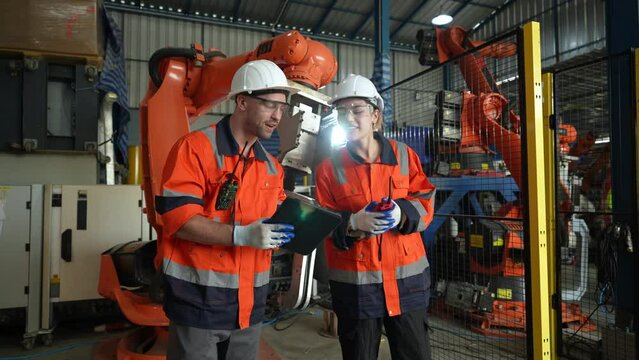 Engineers team use digital tablet computers to control and program robotic arms for production lines.