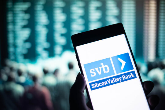 A hand holds a smartphone with the logo of the Silicon Valley Bank on the background of the screen in stock quotes of collapsed shares. The largest bank failure in the US.