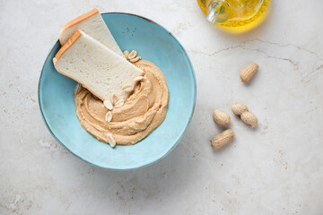 Turquoise bowl with peanut butter and slices of white bread for making sandwiches, top view on a light-beige stone background