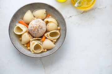 Grey plate with catalan escudella on a light-beige marble background, horizontal shot with copy space, flat lay