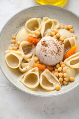 Middle close-up of escudella soup with pasta and pilota served in a beige plate, vertical shot, selective focus