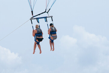 Rear view of two friends parasailing against the blue sky in Mexico