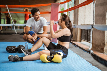 the male boxer talking to the female boxer while sitting and drinking inside the box ring