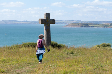 Femme de dos marchant vers une grosse croix en granit, Bretagne