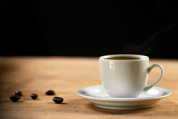 Coffee cup and coffee beans on wooden table. Black background.