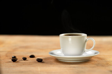 Coffee cup and coffee beans on wooden table. Black background.