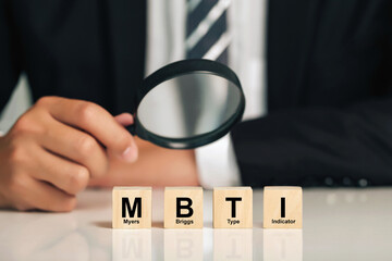businessman holding magnifying glass with wooden cubes with MBTI.Psychological and personality test...