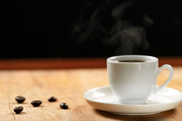 Coffee cup and coffee beans on wooden table. Black background.