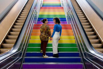 Couple of lesbian girls in love climb the lgtb stairs of lgbt flag on gay pride day