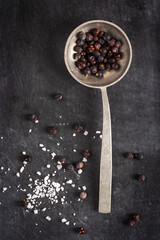 Old spoon with juniper berries and salt pile on black background