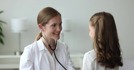Happy friendly pediatrician woman examining little patient girl, applying stethoscope to chest, listening heartbeat, breath, speaking, smiling, giving high five to kid