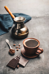 Black coffee drink in a clay cup, turkish jezve coffee pot, chocolate pieces and coffee beans in a spoon on dark background