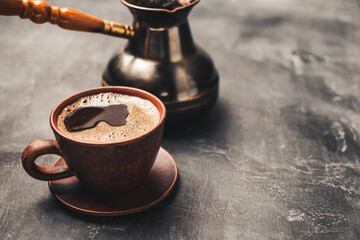 Black coffee drink in a clay cup and turkish jezve coffee pot on dark background