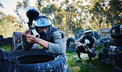 Team, paintball and tires for cover, hiding or protection while firing or aiming down sights together in nature. Group of paintballers waiting in teamwork for opportunity to attack or shoot in sports