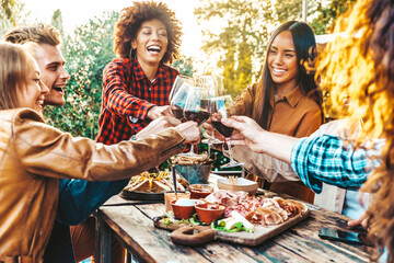 Multiracial friends having fun at barbecue dinner party in garden restaurant - Millennial people cheering red wine sitting at outside bar table - Youth lifestyle, food and beverage concept - obrazy, fototapety, plakaty