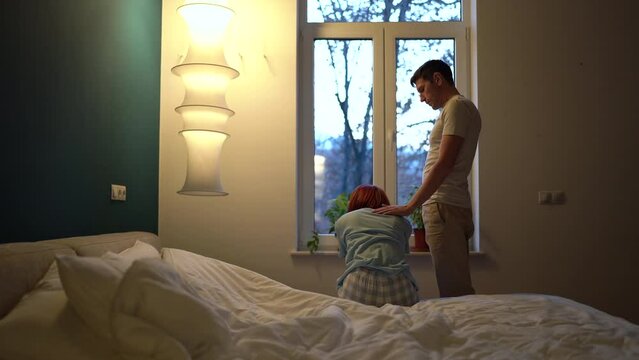 Young loving man husband apologizing to wife during argument, comforting and embracing her while sitting together in bedroom, upset guy feeling guilty, making up with girlfriend after fight