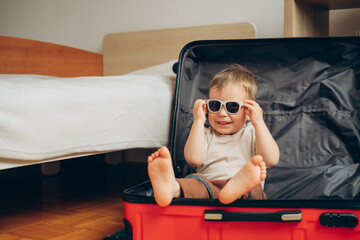 travel concept.  child in sunglasses sits in a red suitcase at the home 