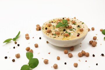Compsition of classic hummus on a white background in a plate topped with chickpeas and sesame seeds, basil and spices. Culinary and food projects photo. Eastern or Mediterranean cuisine