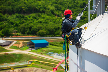 Focus male worker inspection wearing safety first harness rope safety line working at a high tank roof place on pipe