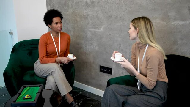 Two coworkers are in the office lobby having a coffee break and talking together.