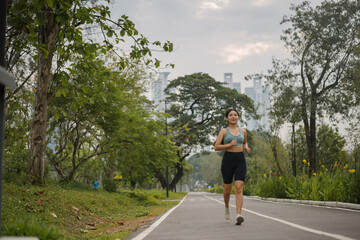 Asian happy woman running in park on morning. Healthy female wearing sportswear and warm-up exercise in outdoors. wellness lifestyle, outside activities.