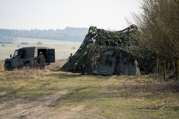 British army camouflaged lean-to vehicle tent by woodland, with a Land Rover Wolf