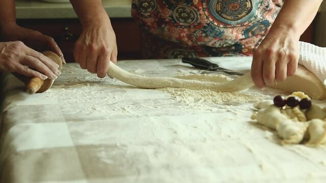 Home cooking of traditional Ukrainian cuisine. Vareniki with cherries close-up. A woman rolls out the dough with a rolling pin and sculpts dumplings.
