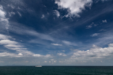 Wide panorama of light clouds in sky over sea with small distant white ship, Thailand