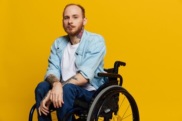 A man in a wheelchair looks at the camera, with tattoos on his arms sits on a yellow studio background, the concept of health is a person with disabilities
