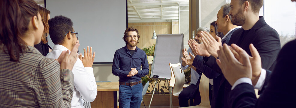 Group of people are greeting man coach standing near flipboard in modern office clapping hands, adult education concept. Office workers on corporative training, team building seminar or master class.