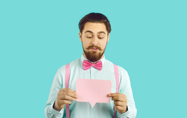 Portrait of a handsome man in a shirt and bow tie holding a rectangular pink mockup speech balloon. Young guy dressed up for a party showing a blank clean paper mock up message bubble