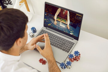 Online casino. Young smart male online poker player relaxing gambling on his laptop computer at home. Concept of online gambling, win money, sports bet, chance, succeed, fortune and addiction.