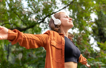 Woman with arms outstretched listens to music in nature.