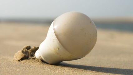 Fototapeta na wymiar Light bulb sticking out of the sand. Concept of pollution