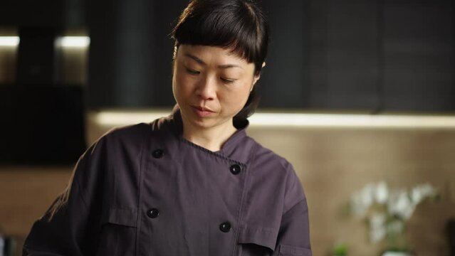 Medium slow-motion shot of a japanese woman slicing sweet red bell pepper on a wooden cutting board in the kitchen