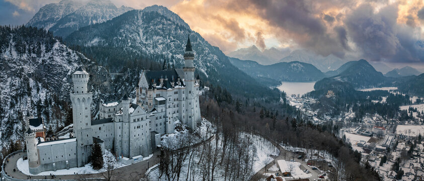 Aerial view of the Neuschwanstein Castle or Schloss Neuschwanstein on a winter day, with the mountains and trees capped with snow all around it.
