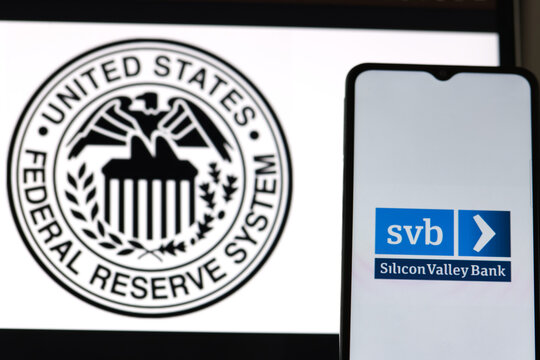 Smartphone with SVB - Silicone Valley Bank logo on mobile phone and Federal Reserve symbol on computer screen, USA, 12 March 2023