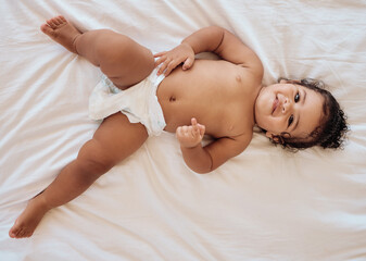 Happy baby, smile and relax on bed in family home bedroom for diaper change, bedtime or healthy...