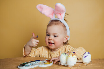 A child with bunny ears on his head paints Easter eggs.