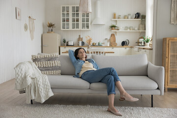 Obraz premium Calm sleepy middle aged woman resting on soft couch with closed eyes, stretching body, enjoying comfort, leisure time, laziness at home, meditating, breathing fresh air