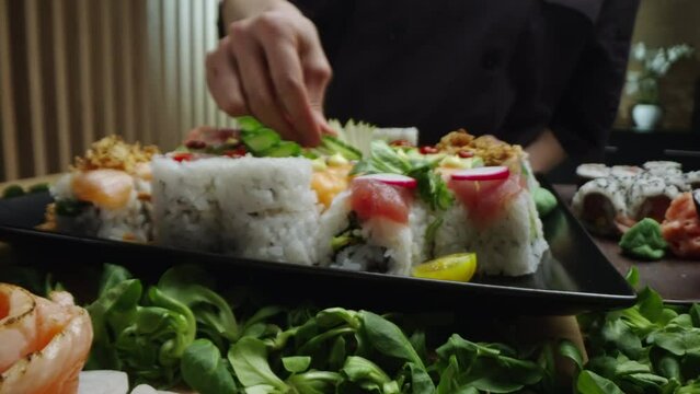 Extreme close-up shot of a female sushi chef putting cucumber piece on sushi decorated beautifully on tray in slow-motion. Close-up on chef hands
