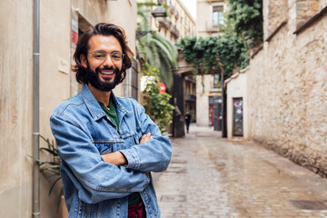 Fototapeta na wymiar smiling caucasian man with arms crossed in a nice old street with plants, concept of lifestyle and youth, copy space for text