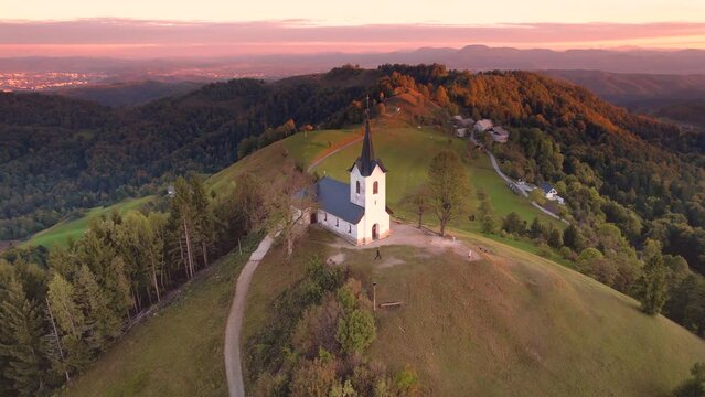 Aerial view of a colourful autumn sunset at Church of Saint Jacob (Sveti Jakob) in Medvode. Snowcapped mountains with the Karawanks, the Julian Alps and the Triglav, Medvode, Ljubljana, Slovenia
