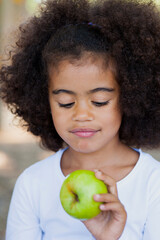 Close up portrait of little girl holding green apple outdoors in playground.