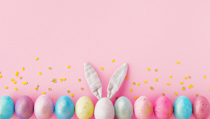 Bunny ears and festive colorful Easter eggs decorated golden confetti on pink background top view..