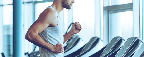 Close-up of young man in sportswear running on treadmill at gym