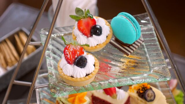 Woman hand delicately take a bright colored macaron from a tower of sweets at a high tea table in a fancy restaurant. Colorful delicious sweet food. Traditional Afternoon tea. Close up.