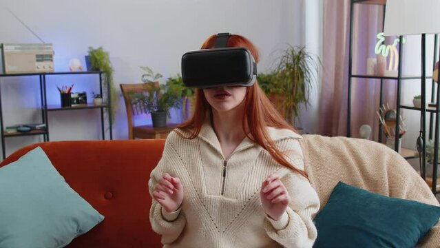 Woman using virtual reality futuristic technology VR app headset helmet to play simulation 3D video game, watching film movie at modern home apartment. Girl in goggles on sofa. Zoom effect transition