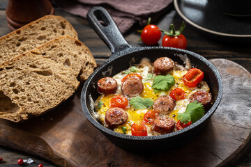 Fried eggs with spicy sausages in a cast-iron frying pan and bread, rustic style - 580097172