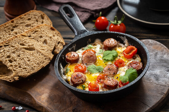 Fried eggs with spicy sausages in a cast-iron frying pan and bread, rustic style